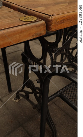 Wooden tables and ornate cast iron chairs stand on a cobblestone patio Wooden tables and ornate cast iron chairs stand on a cobblestone patio 125893069