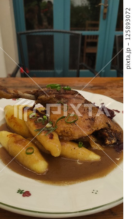 Succulent roasted duck leg served on a plate with golden crispy potatoes and rich savory gravy garnished with fresh green onions inviting culinary delight Succulent roasted duck leg served on a plate with golden crispy potatoes and rich savory gravy garnished with fresh green onions inviting culinary delight 125893072