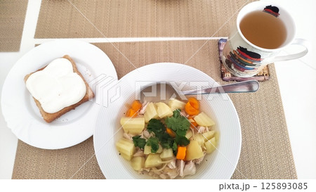 Chicken soup with potatoes, carrots and coriander, bread and herbal tea for healthy lunch dinner Chicken soup with potatoes, carrots and coriander, bread and herbal tea for healthy lunch dinner 125893085