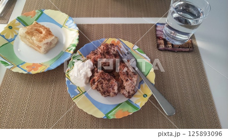 Apple pie and biscuits with cream, served on colorful plates with a glass of water 125893096