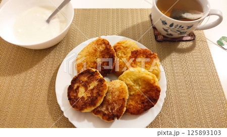 Syrniki, cottage cheese pancakes with sour cream and tea on tablecloth for breakfast 125893103