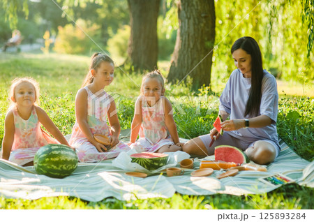 A family in the park, a mother and her children eating watermelon. A healthy lifestyle. 125893284