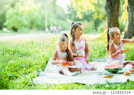 Happy cheerful children eating watermelon in the garden. Cute European little girl eating watermelon fresh fruit in the garden. Happy cheerful children eating watermelon in the garden. Cute European little girl eating watermelon fresh fruit in the garden. 125893314
