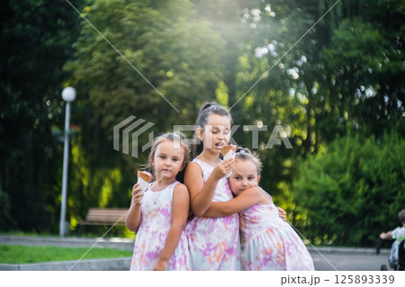 Three sisters stand side by side in a park enjoying an ice cream. Three sisters stand side by side in a park enjoying an ice cream. 125893339