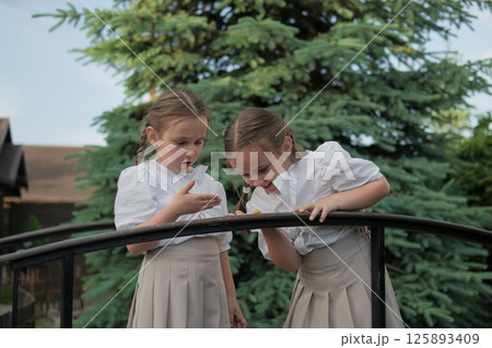 The girls' eyes are fixed on a tiny snail. The braids tied with ribbons complete the image of natural charm. The girls' eyes are fixed on a tiny snail. The braids tied with ribbons complete the image of natural charm. 125893409