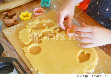 子供がハートの型でクッキー生地を型抜きしているところ。手作りクッキーを作っている工程。 125895032