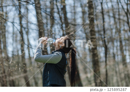 A young woman drinking water in the forest. A woman resting in a park and drinking mineral water from a plastic bottle. A young woman drinking water in the forest. A woman resting in a park and drinking mineral water from a plastic bottle. 125895287