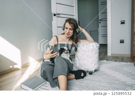 woman enjoying music and browsing on her phone with her dog by her side in a cozy, sunlit room woman enjoying music and browsing on her phone with her dog by her side in a cozy, sunlit room 125895532