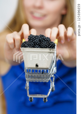 Girl holds blackberry fruits in shopping cart Girl holds blackberry fruits in shopping cart 125896859