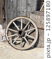 An old wooden cart wheel on the background of a wooden bucket and a door. Antique, vintage items. Old transport 125897180