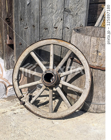 An old wooden cart wheel on the background of a wooden bucket and a door. Antique, vintage items. Old transport An old wooden cart wheel on the background of a wooden bucket and a door. Antique, vintage items. Old transport 125897180