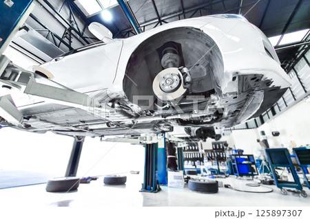 White vehicle elevated on a lift in a auto repair garage with removed wheels White vehicle elevated on a lift in a auto repair garage with removed wheels 125897307