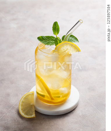 Iced tea with lemon and mint in a glass on a light background with citrus slice. Iced tea with lemon and mint in a glass on a light background with citrus slice. 125897584