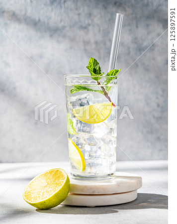 Mojito cocktail in a tall glass with lime, mint and ice on a marble stand on a light background 125897591
