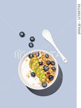 Natural yogurt with granola, kiwi and blueberries in a bowl on a blue background with berries. Natural yogurt with granola, kiwi and blueberries in a bowl on a blue background with berries. 125897592