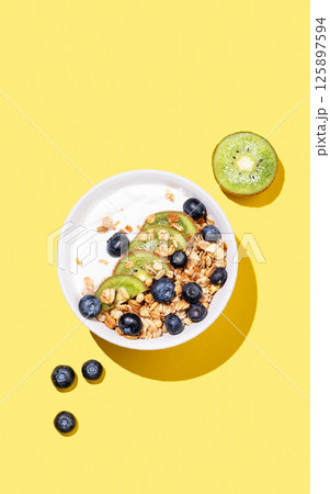 Natural yogurt with granola, kiwi and blueberries in a bowl on a bright yellow background Natural yogurt with granola, kiwi and blueberries in a bowl on a bright yellow background 125897594