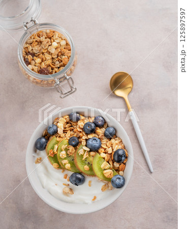 Natural yogurt with granola, kiwi and blueberries in a bowl on a light background with spoon Natural yogurt with granola, kiwi and blueberries in a bowl on a light background with spoon 125897597