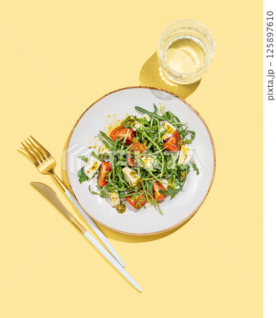 Fresh arugula salad with cherry tomatoes, mozzarella, pesto sauce on yellow background 125897610