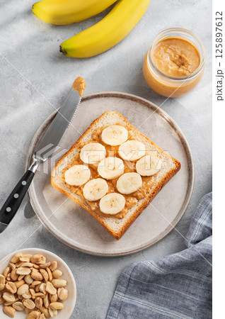 Peanut butter and banana toast on a plate on a light background with morning shadow. 125897612