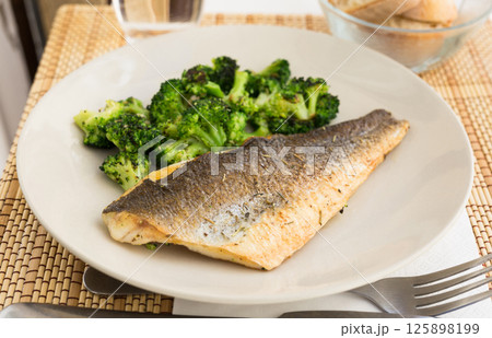 Fried fillet of sea bass with garnish of broccoli on black warm stone plate Fried fillet of sea bass with garnish of broccoli on black warm stone plate 125898199