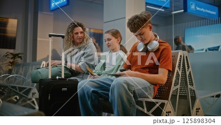 Airport Terminal: Woman with Two Teenage Children Sitting in Departure Lounge After Passport Control 125898304