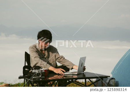 Young business man working computer on peak hill. Hiker online shopping on laptop at sunset, sunrise on top mountain, freelance person remote work with digital tablet. travel vacation holiday concept Young business man working computer on peak hill. Hiker online shopping on laptop at sunset, sunrise on top mountain, freelance person remote work with digital tablet. travel vacation holiday concept 125898314