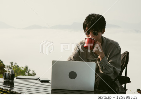 Young business man working computer on peak hill. Hiker online shopping on laptop at sunset, sunrise on top mountain, freelance person remote work with digital tablet. travel vacation holiday concept Young business man working computer on peak hill. Hiker online shopping on laptop at sunset, sunrise on top mountain, freelance person remote work with digital tablet. travel vacation holiday concept 125898315