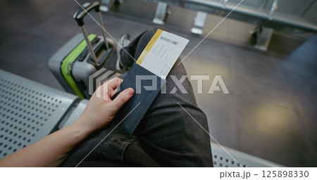 Airport Terminal: Passenger with Suitcase Sitting in Departure Lounge of Airline Hub. First-Person View Airport Terminal: Passenger with Suitcase Sitting in Departure Lounge of Airline Hub. First-Person View 125898330