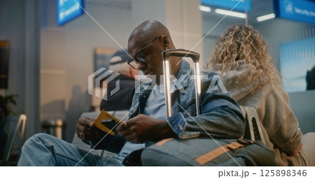 Man with Luggage Sitting and Waiting for Flight, Using Smartphone in Departure Lounge of Crowded Airline Hub 125898346