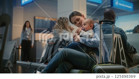 Airport Terminal: Adult Woman Sitting with Infant and Waiting for Airplane Flight Airport Terminal: Adult Woman Sitting with Infant and Waiting for Airplane Flight 125898369