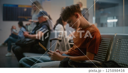 Diverse Passengers in Departure Lounge of Airline Hub. Teenage Boy Using Smartphone 125898416