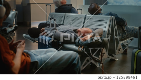 Exhausted Man with Luggage Sleeping on the Seats in Boarding Lounge of Airline Hub Exhausted Man with Luggage Sleeping on the Seats in Boarding Lounge of Airline Hub 125898461