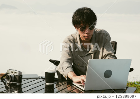 Young business man working computer on peak hill. Hiker online shopping on laptop at sunset, sunrise on top mountain, freelance person remote work with digital tablet. travel vacation holiday concept 125899097