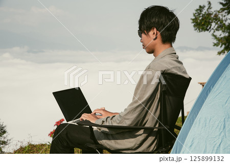 Young business man working computer on peak hill. Hiker online shopping on laptop at sunset, sunrise on top mountain, freelance person remote work with digital tablet. travel vacation holiday concept 125899132
