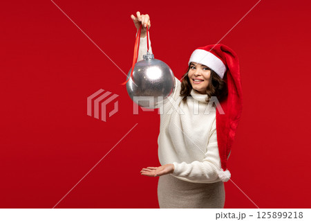 Woman in Santa hat lifting large silver Christmas ornament. Woman in Santa hat lifting large silver Christmas ornament. 125899218