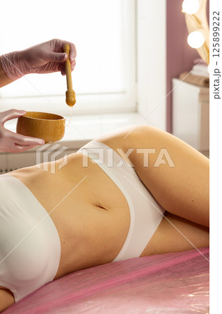 Spa practitioner dripping honey on stomach during skin treatment. Spa practitioner dripping honey on stomach during skin treatment. 125899222