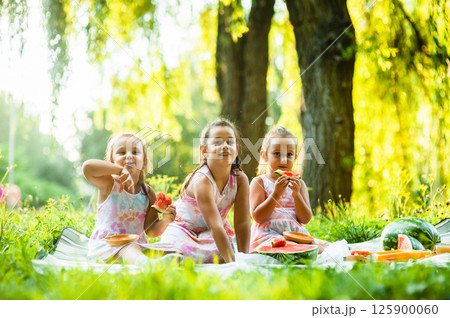 The sisters are sitting together enjoying a delicious watermelon in the open air. 125900060