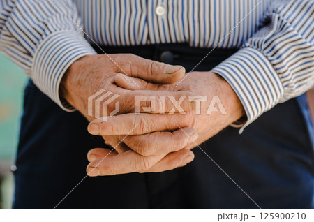 The old man's hands are folded into a lock. His aged fingers tell of past trials. 125900210
