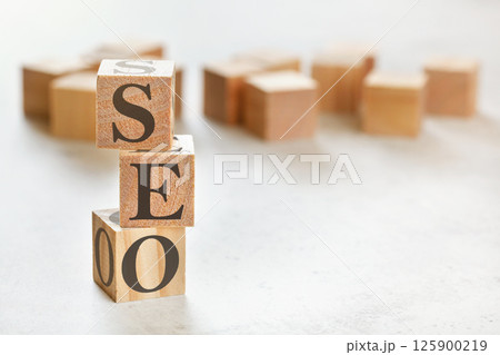 Three wooden cubes with letters SEO (means Search Engine Optimization), on white table, more in background, space for text in right down corner 125900219