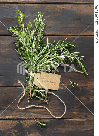Fresh green rosemary sprigs with kraft paper text label dark weathered wooden table top view Fresh green rosemary sprigs with kraft paper text label dark weathered wooden table top view 125901300