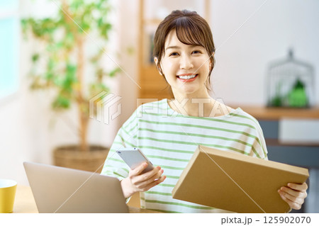 リビングでメール便の荷物を確認するスマホを持った若い女性 125902070
