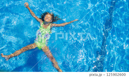 Child enjoys sunny day while floating in a swimming pool with clear blue water during summer Child enjoys sunny day while floating in a swimming pool with clear blue water during summer 125902600