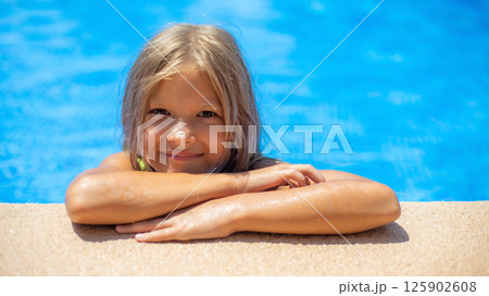Young child enjoys sunny day at poolside with sparkling water in the background during summer 125902608