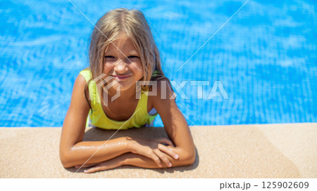 Young girl enjoying a sunny day at the pool, smiling with joy while leaning on the edge of the water 125902609