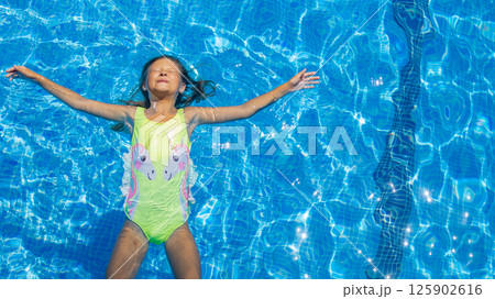 Child enjoys a sunny day floating in a bright blue swimming pool during summer Child enjoys a sunny day floating in a bright blue swimming pool during summer 125902616