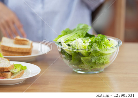 Close up fresh salad on wooden table in bright indoor setting. Couple enjoying healthy breakfast with sandwiches. Close up fresh salad on wooden table in bright indoor setting. Couple enjoying healthy breakfast with sandwiches. 125903031
