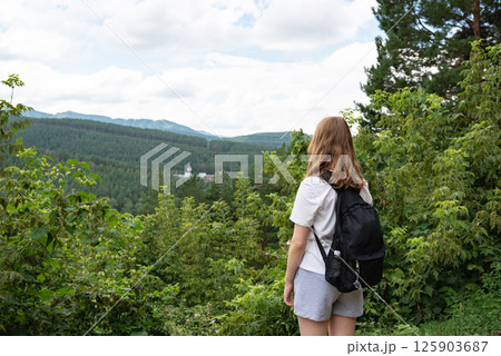 Woman hiker standing on mountain trail, looking at forested hills. Woman hiker standing on mountain trail, looking at forested hills. 125903687