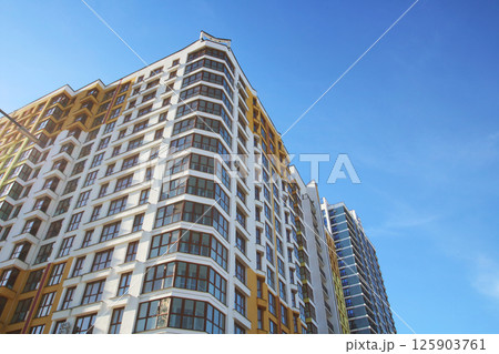 Gazing up at a towering building against a backdrop of bright blue sky 125903761