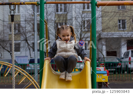 A cheerful little girl with pigtails, enjoying playing time on a hill on a city gaming platform, plunging into the delightful experience of children's joy and laughter. 125903843
