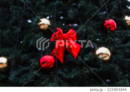 Close-up view of a beautifully decorated christmas tree featuring a vibrant red bow and shiny gold and red ornaments, creating an inviting, festive atmosphere perfect for the holiday season. 125903844